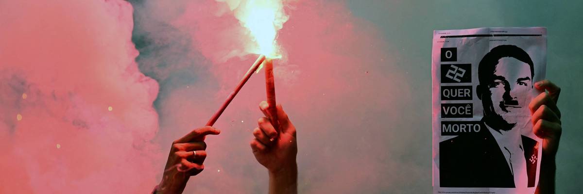 Protesters hold flares and an image of Flavio Bolsonaro as Hitler.