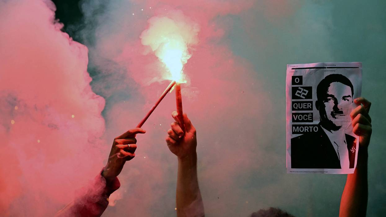 Protesters hold flares and an image of Flavio Bolsonaro as Hitler.