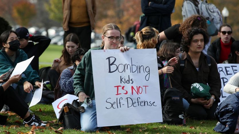 Protesters hold placards as they sit outside of a campus...