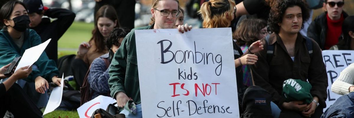 Protesters hold placards as they sit outside of a campus...