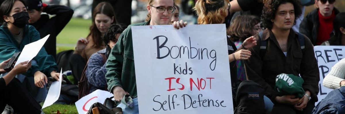 Protesters hold placards as they sit outside of a campus...