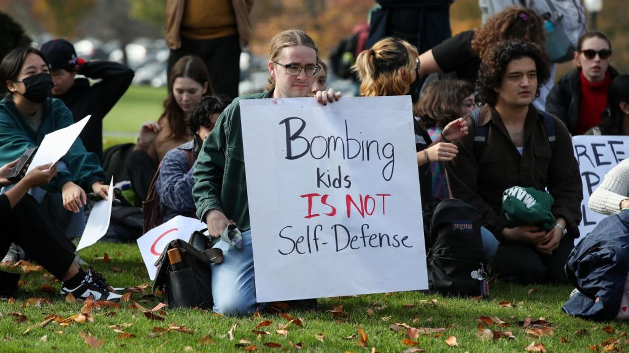 Protesters hold placards as they sit outside of a campus...
