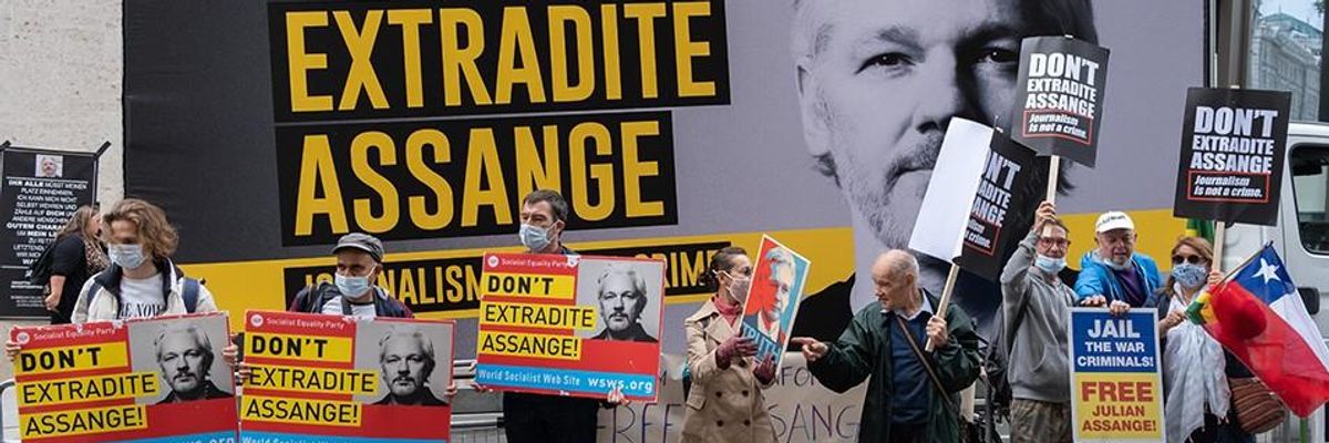 Protesters hold signs reading "Don't Extradite Assange" in front of a large sign with his photo.