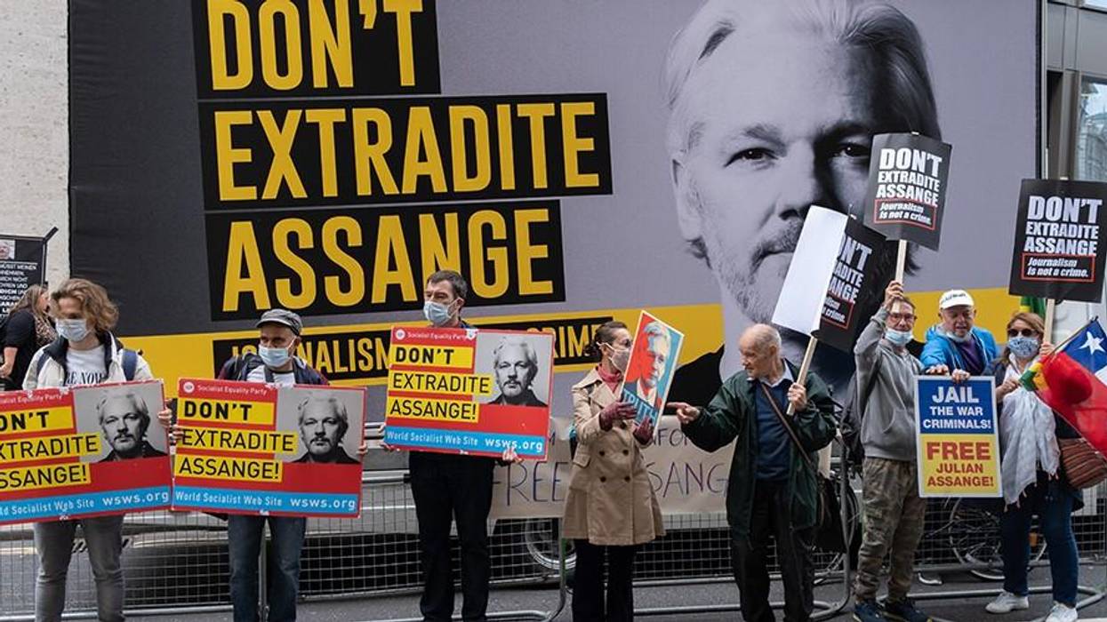 Protesters hold signs reading "Don't Extradite Assange" in front of a large sign with his photo.