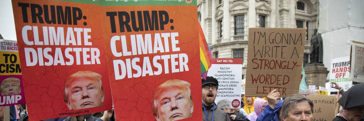 Protesters hold signs reading, "Trump: Climate Disaster."