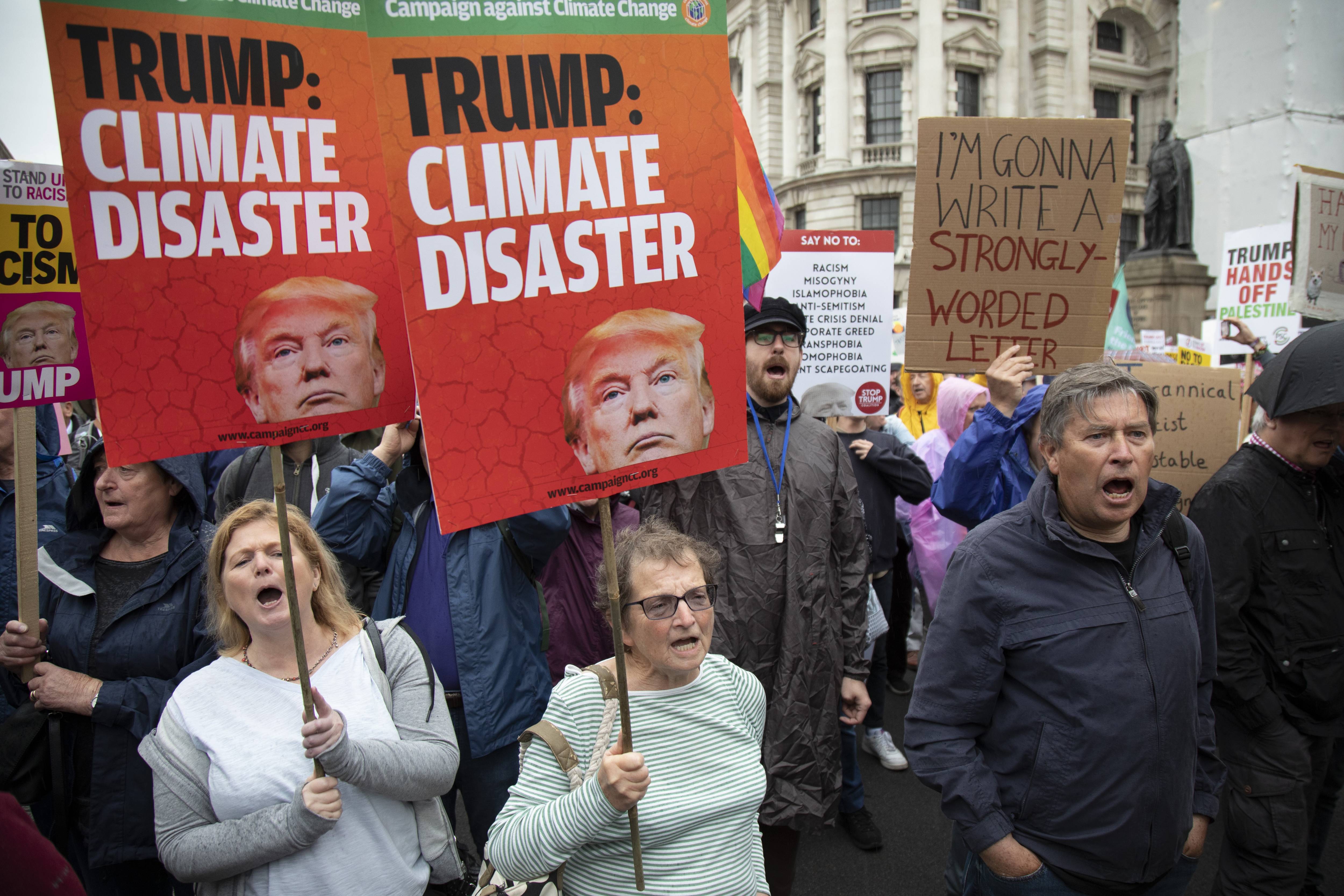 Protesters hold signs reading, "Trump: Climate Disaster."
