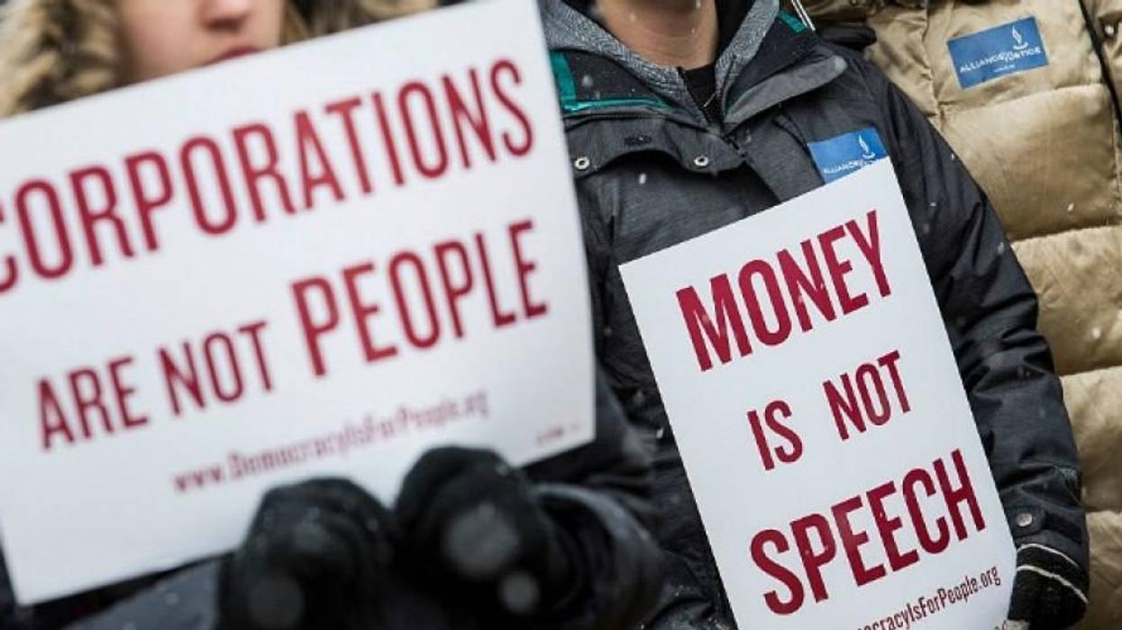 Protesters hold signs saying, "Corporations are not people" and "Money is not speech."