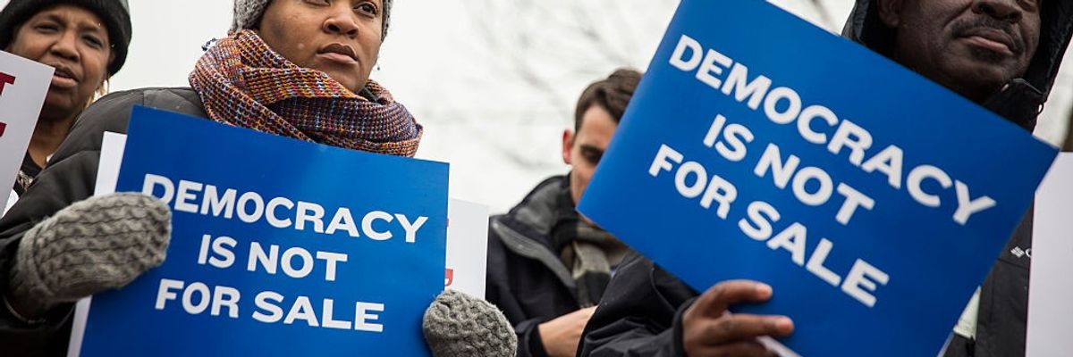 Protesters hold signs saying, "Democracy is not for sale."