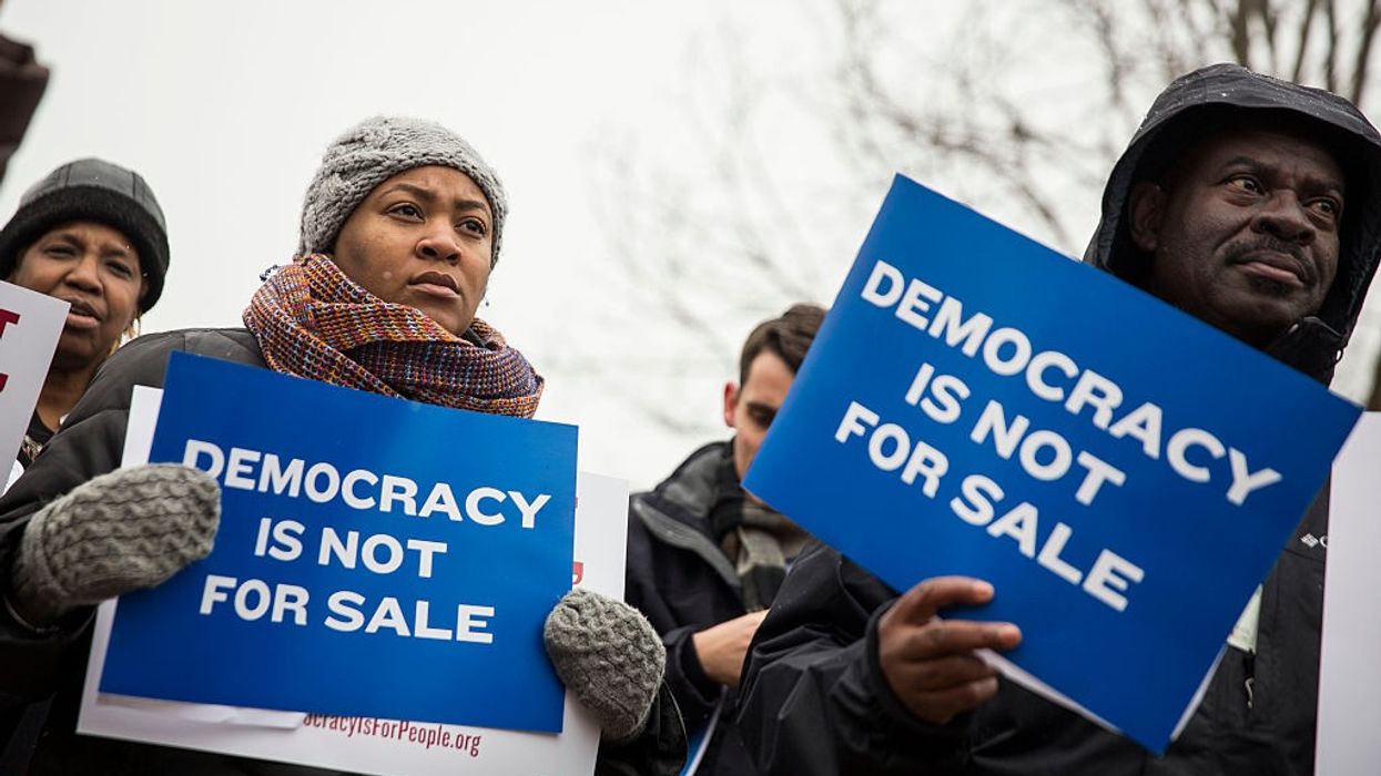 Protesters hold signs saying, "Democracy is not for sale."