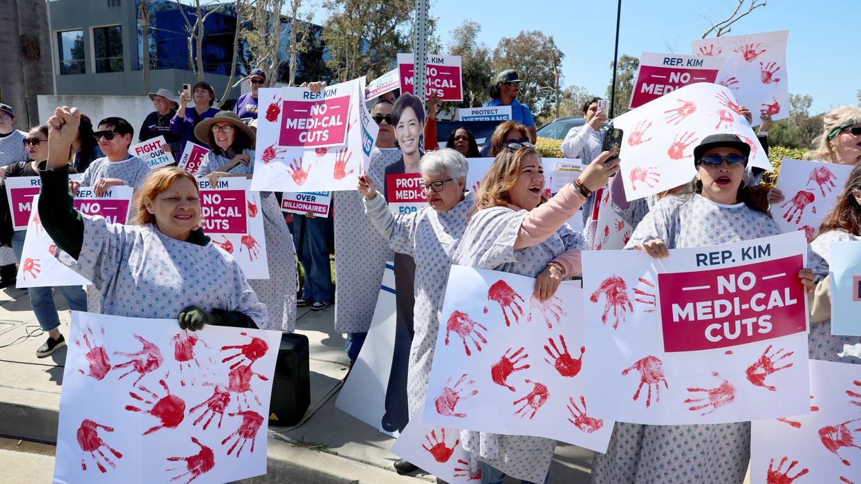 Protesters in hospital gowns hold signs reading, "No Medicaid cuts."