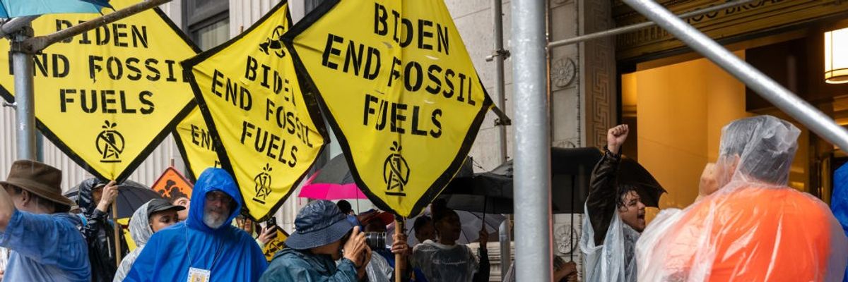 Protesters in raincoats hold yellow signs calling for an end to fossil fuels. 