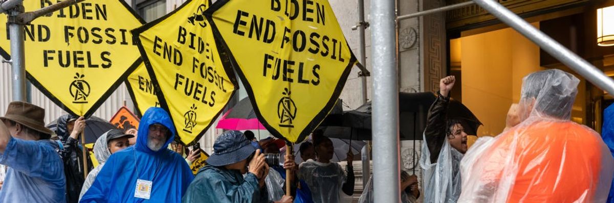 Protesters in raincoats hold yellow signs calling for an end to fossil fuels. 