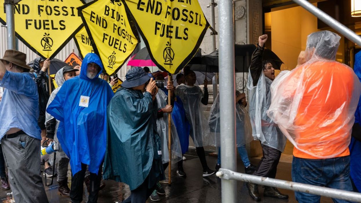 Protesters in raincoats hold yellow signs calling for an end to fossil fuels.