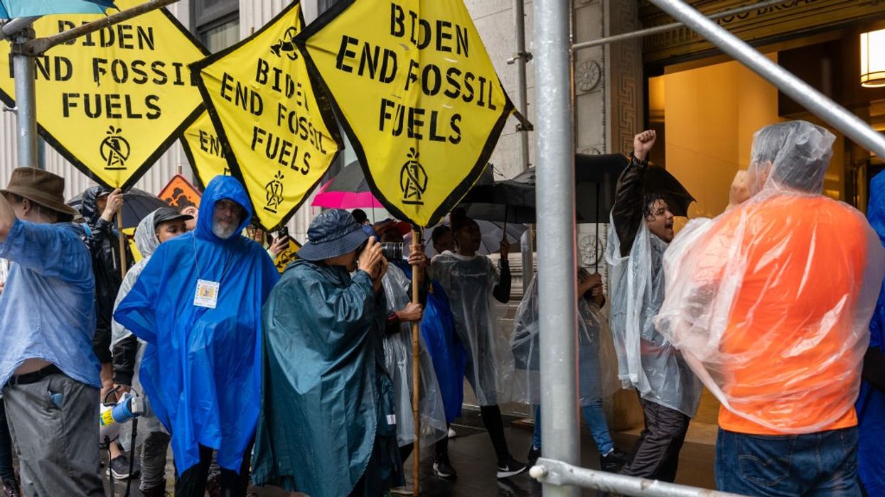 Protesters in raincoats hold yellow signs calling for an end to fossil fuels.