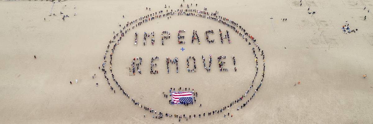 Protesters in sand form words, "Impeach + Remove."