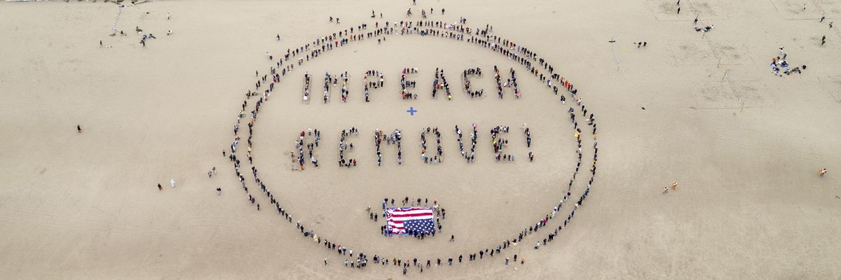 Protesters in sand form words, "Impeach + Remove."