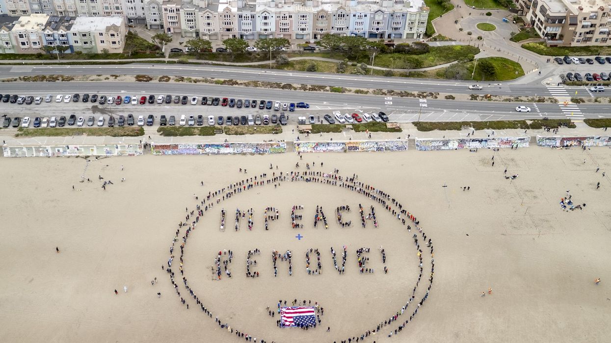 Protesters in sand form words, "Impeach + Remove."
