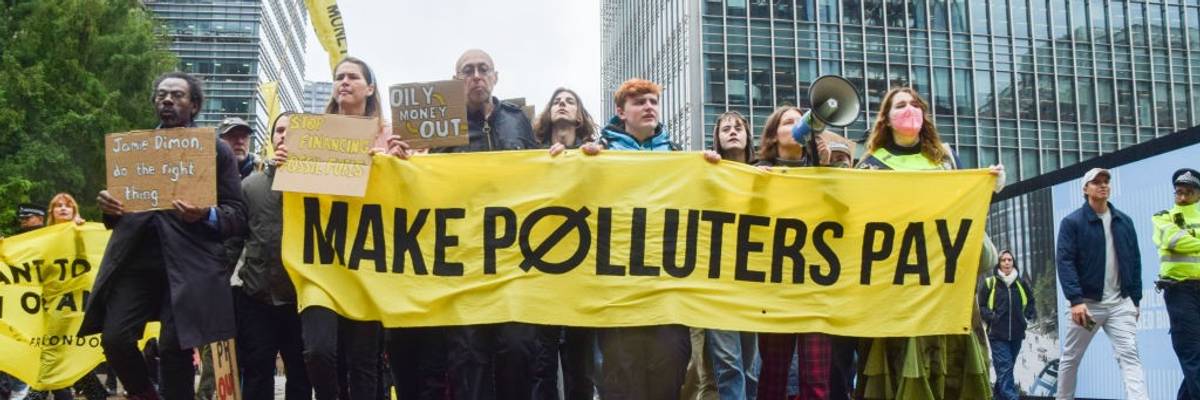 Protesters march with a banner which states 'Make polluters...