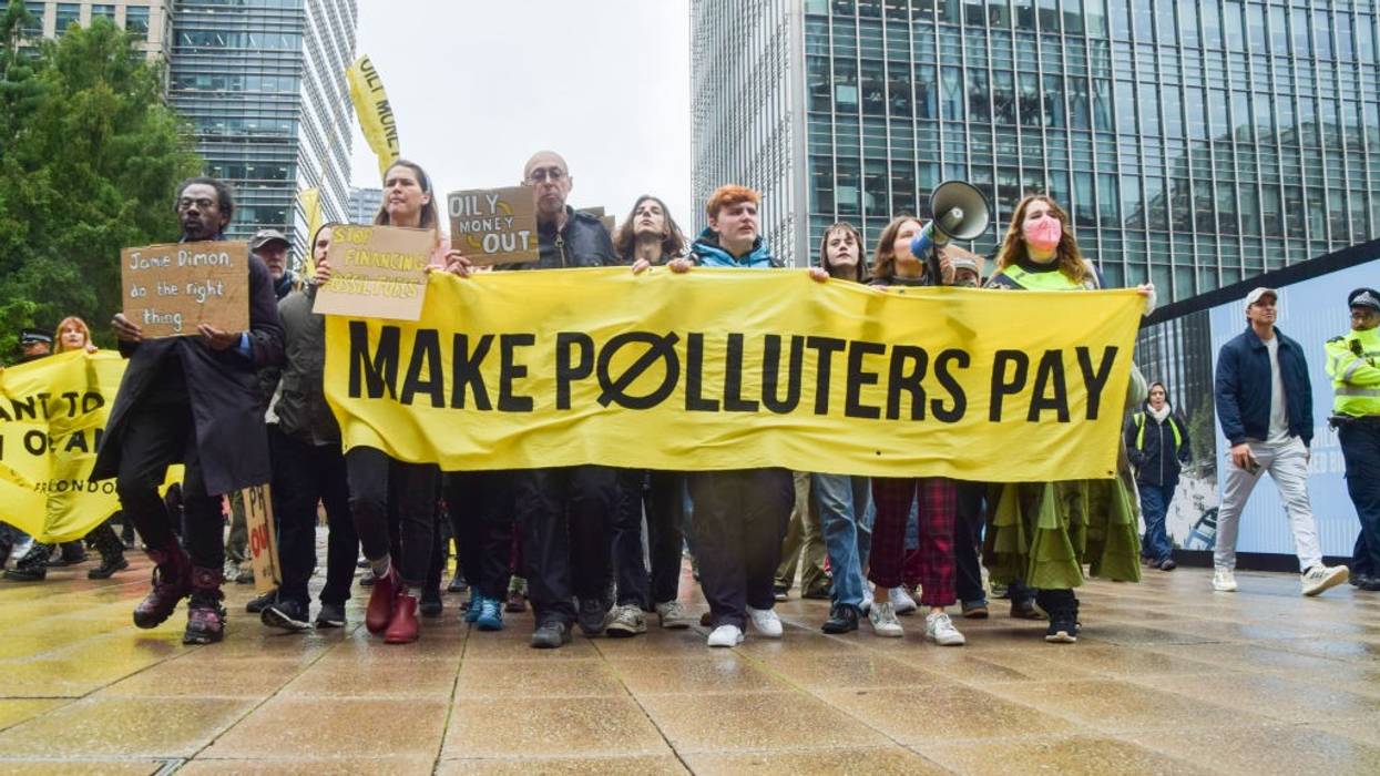 Protesters march with a banner which states 'Make polluters...