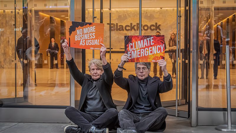 Protesters sit outside BlackRock H!Q holding signs reading, "No more business as usual" and "Climate emergency."