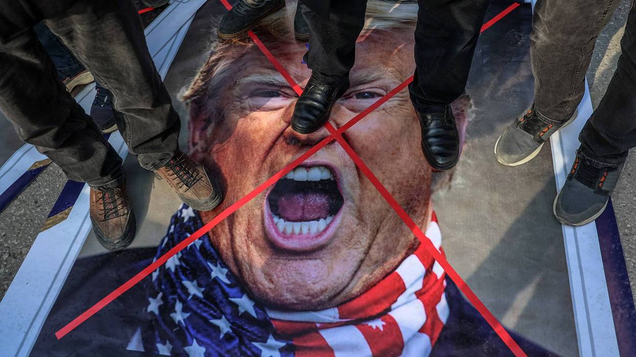 Protesters stand on an image of Trump.
