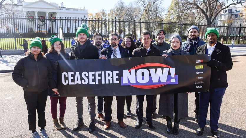 Protesters stand outside the White House with a sign saying, "Ceasefire now!"