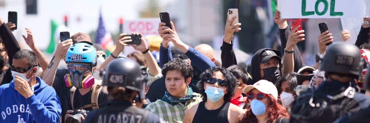 protestors and a member of the media stand across from police