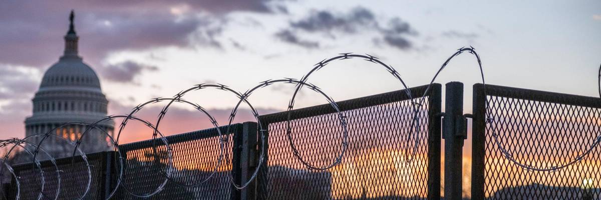 Razor wire and a fence around the Capitol building at sunrise.