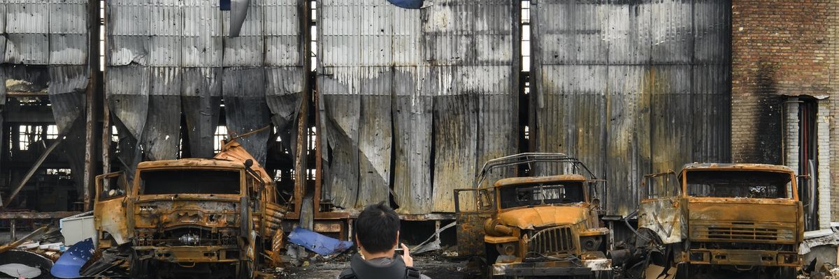 Reporter standing before burned out trucks during war in Ukraine
