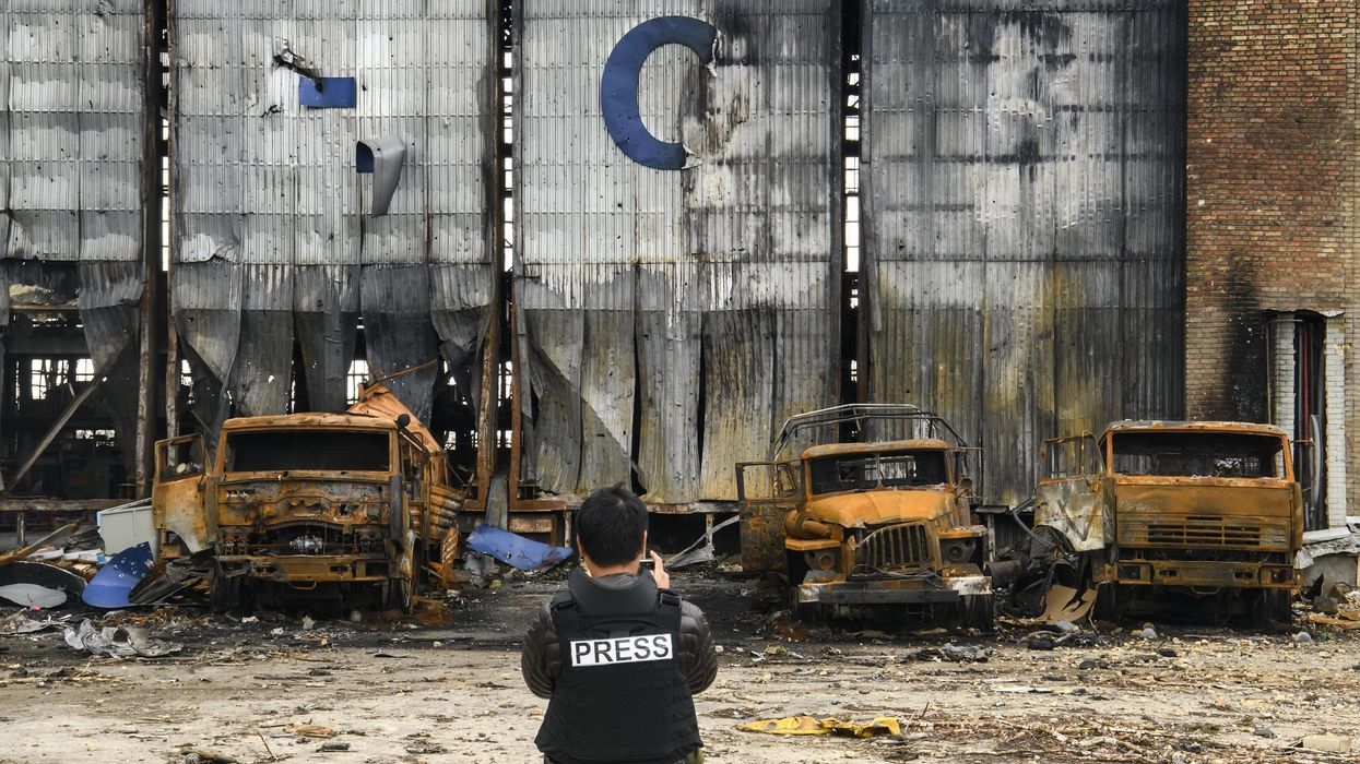 Reporter standing before burned out trucks during war in Ukraine