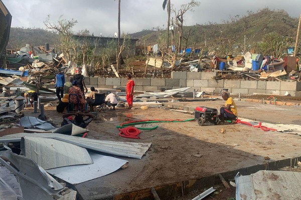 residents sitting among piles of debris of metal sheets and wood after homes were destroyed by the cyclone Chido
