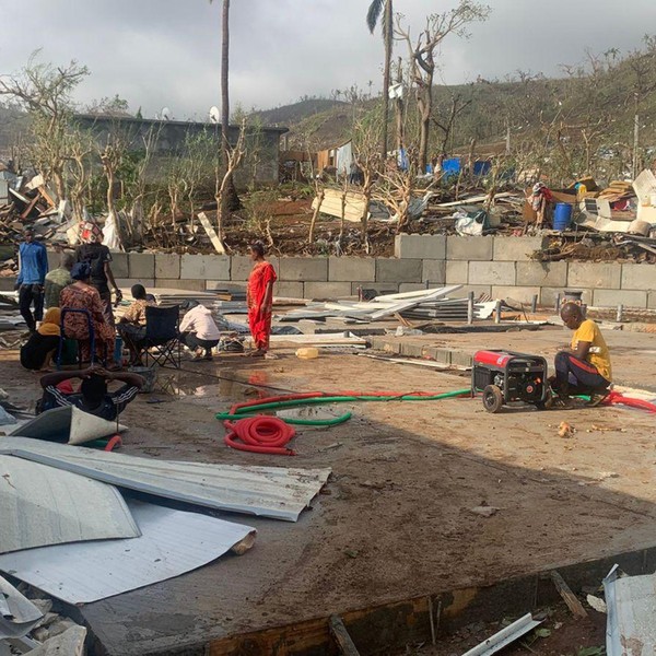 residents sitting among piles of debris of metal sheets and wood after homes were destroyed by the cyclone Chido