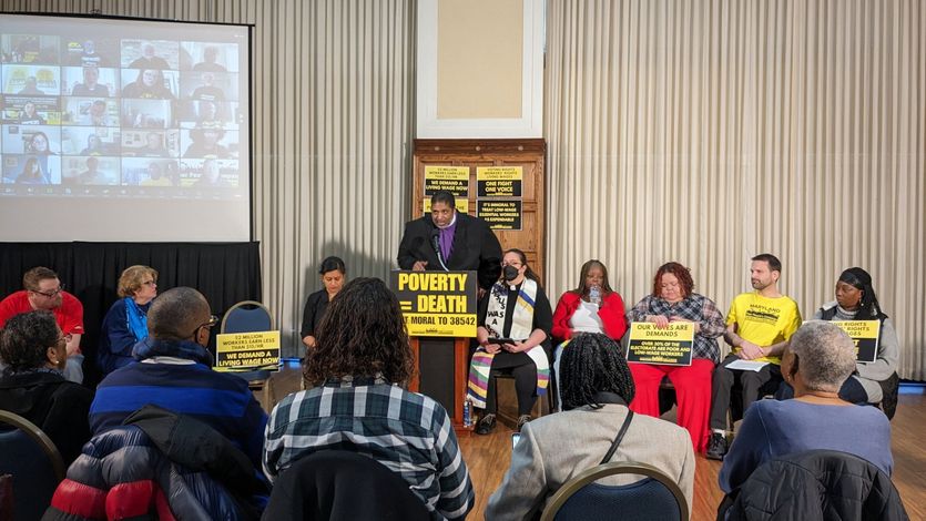 Rev. Dr. William Barber speaks at a podium with a sign reading "Poverty = Death."