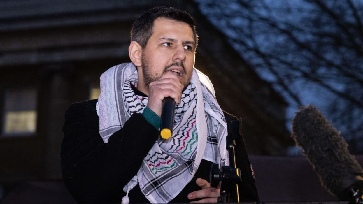 Richard Medhurst speaks wearing a keffiyeh