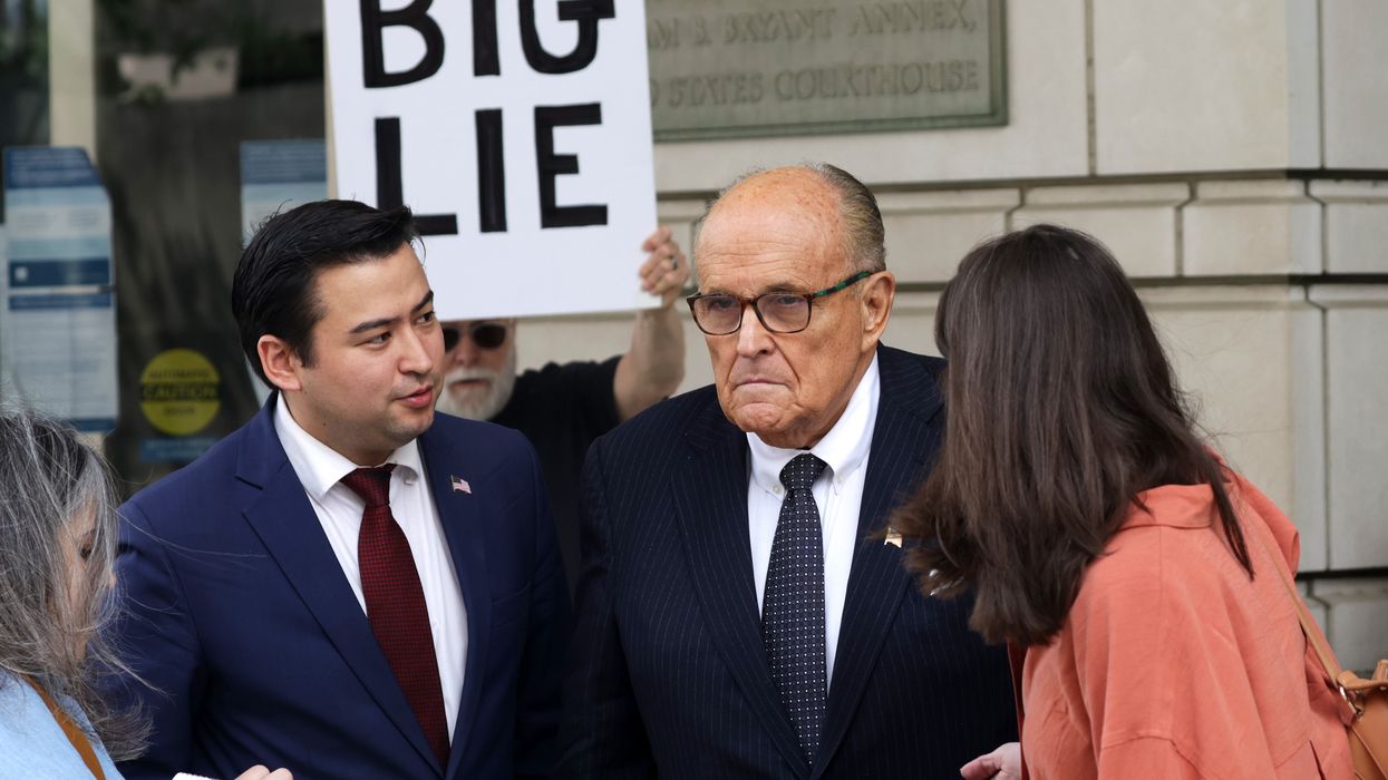 Rudy Giuliani talks to the press while a protester holds a sign reading, "Big Lie"