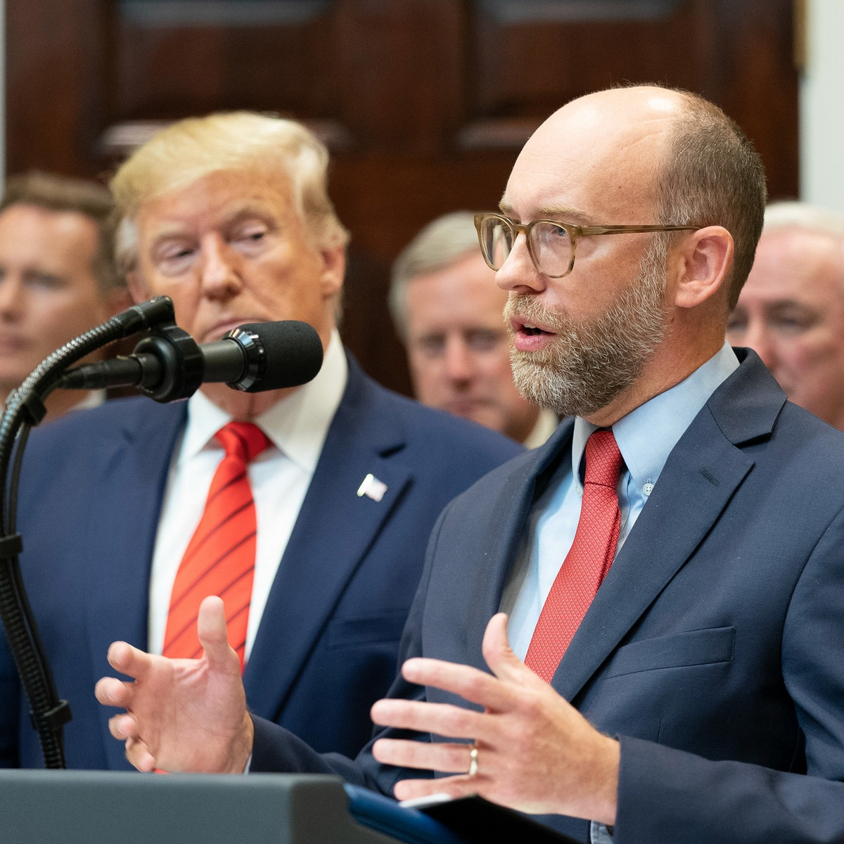 Russ Vought speaks while Donald Trump looks on