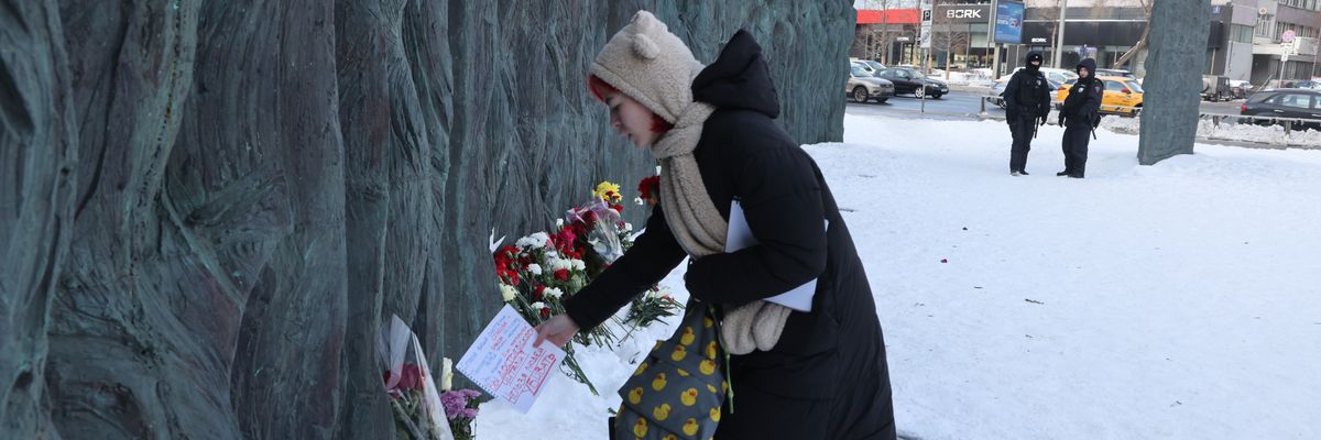 Russian police look on as a woman brings a carnation and a small text about opposition leader Alexei Navalny to the Wall of Grief
