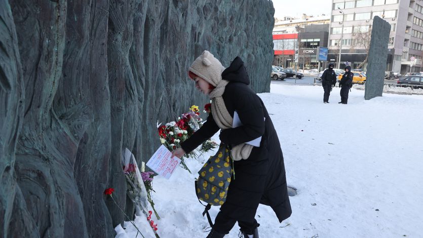 Russian police look on as a woman brings a carnation and a small text about opposition leader Alexei Navalny to the Wall of Grief