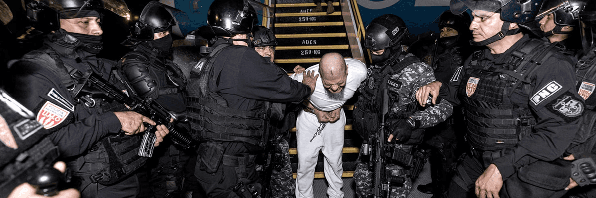 Salvadoran security forces in black riot gear remove a prisoner from a deportation flight from the US