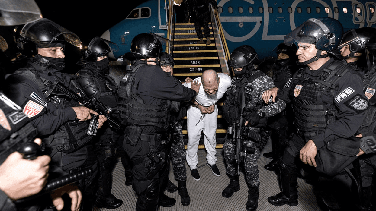 Salvadoran security forces in black riot gear remove a prisoner from a deportation flight from the US