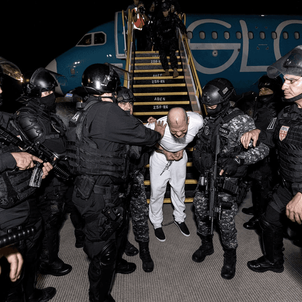 Salvadoran security forces in black riot gear remove a prisoner from a deportation flight from the US