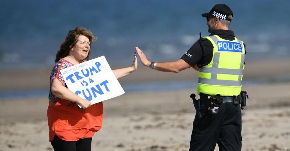 Scottish stand-up comedian Janey Godley gives a high-five to a police officer as she holds a sign in protest stating 'Trump is a runt' on the beach outside near Trump Turnberry Luxury Collection Resort during the U.S. President's visit to the United Kingdom on July 14, 2018 in Turnberry, Scotland. The President of the United States and First Lady, Melania Trump on their first official visit to the UK after yesterday's meetings with the Prime Minister and the Queen is in Scotland for private weekend stay at his Turnberry. (Photo: Leon Neal/Getty Images)