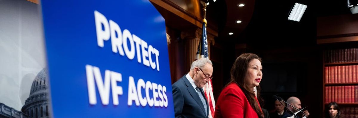 Sen. Tammy Duckworth speaks in a red suit by a sign reading "Protect IVF Access for All."