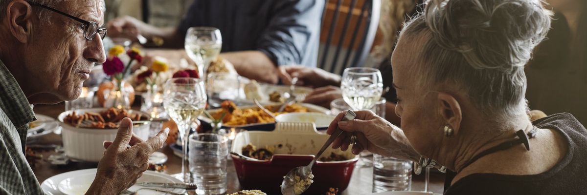 Senior man looking at woman serving food while sitting at Thanksgiving dinner