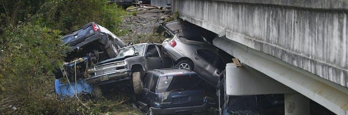 Several cars and a large pickup truck are piled up against a bridge after being swept downstream by a flood.