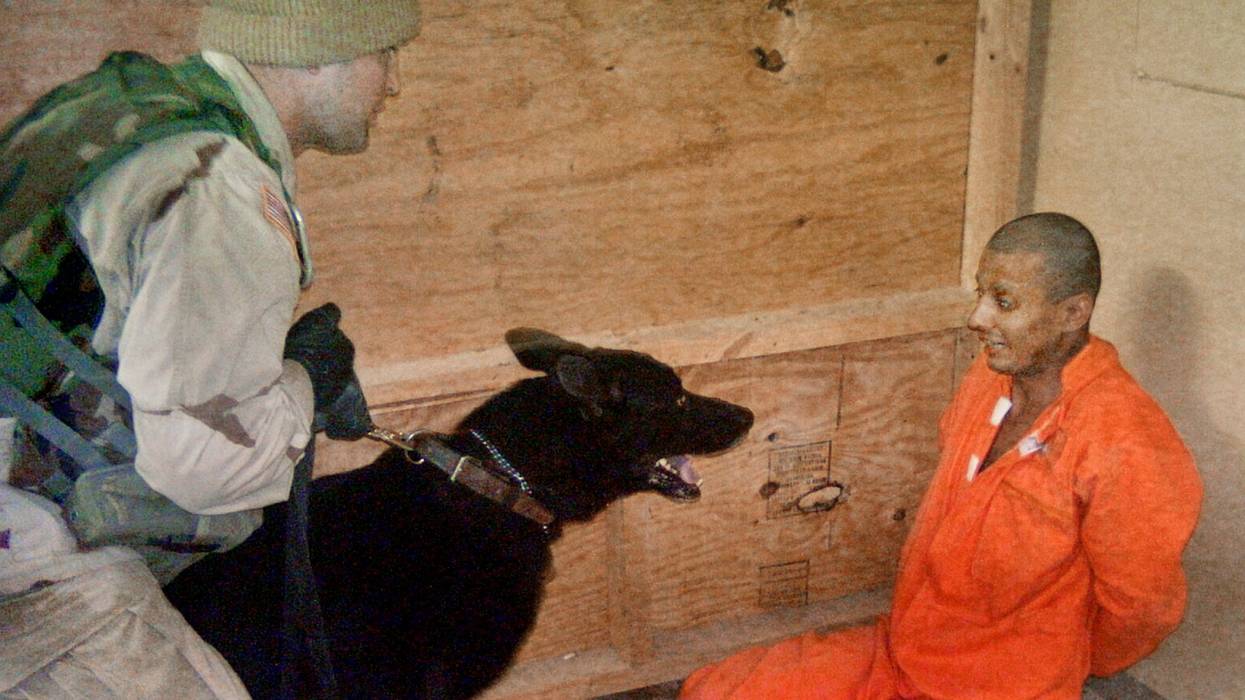 Sgt. Michael Smith uses a dog to torture a terrified Abu Ghraib prisoner in an orange jumpsuit.