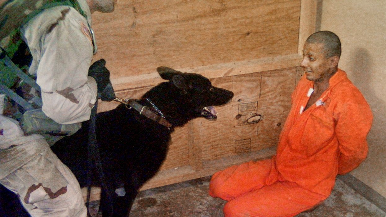 Sgt. Michael Smith uses a dog to torture a terrified Abu Ghraib prisoner in an orange jumpsuit.