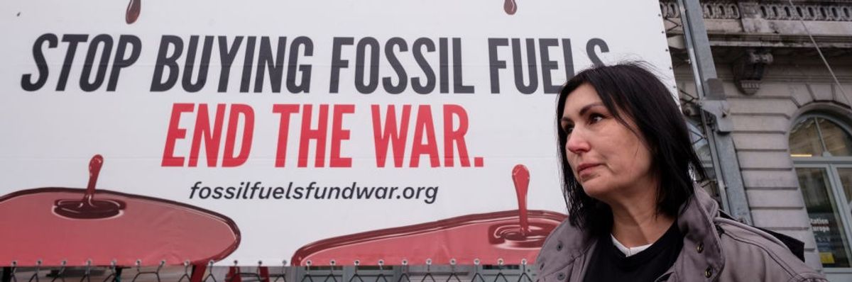Sign says behind activist Svitlana Romanko says "Stop buying fossil fuels. End the War."
