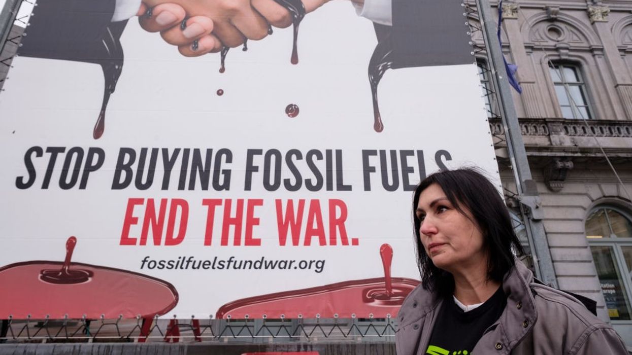 Sign says behind activist Svitlana Romanko says "Stop buying fossil fuels. End the War."