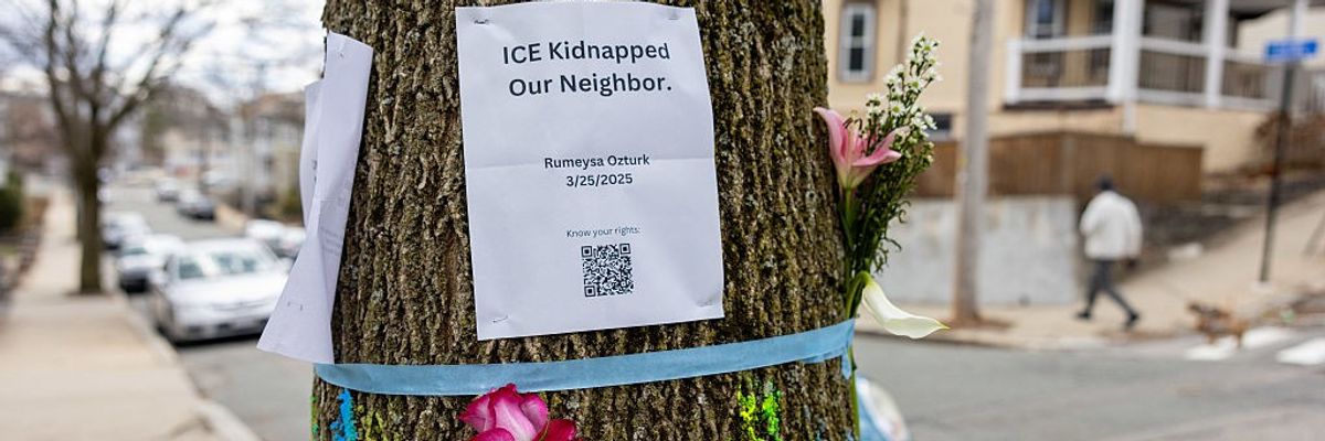 Signage and flowers are placed on a tree next to where ICE agents apprehended Rumeysa Ozturk